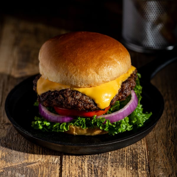 Cheeseburger with lettuce, tomato, and red onion in a cast iron pan on a wooden table.