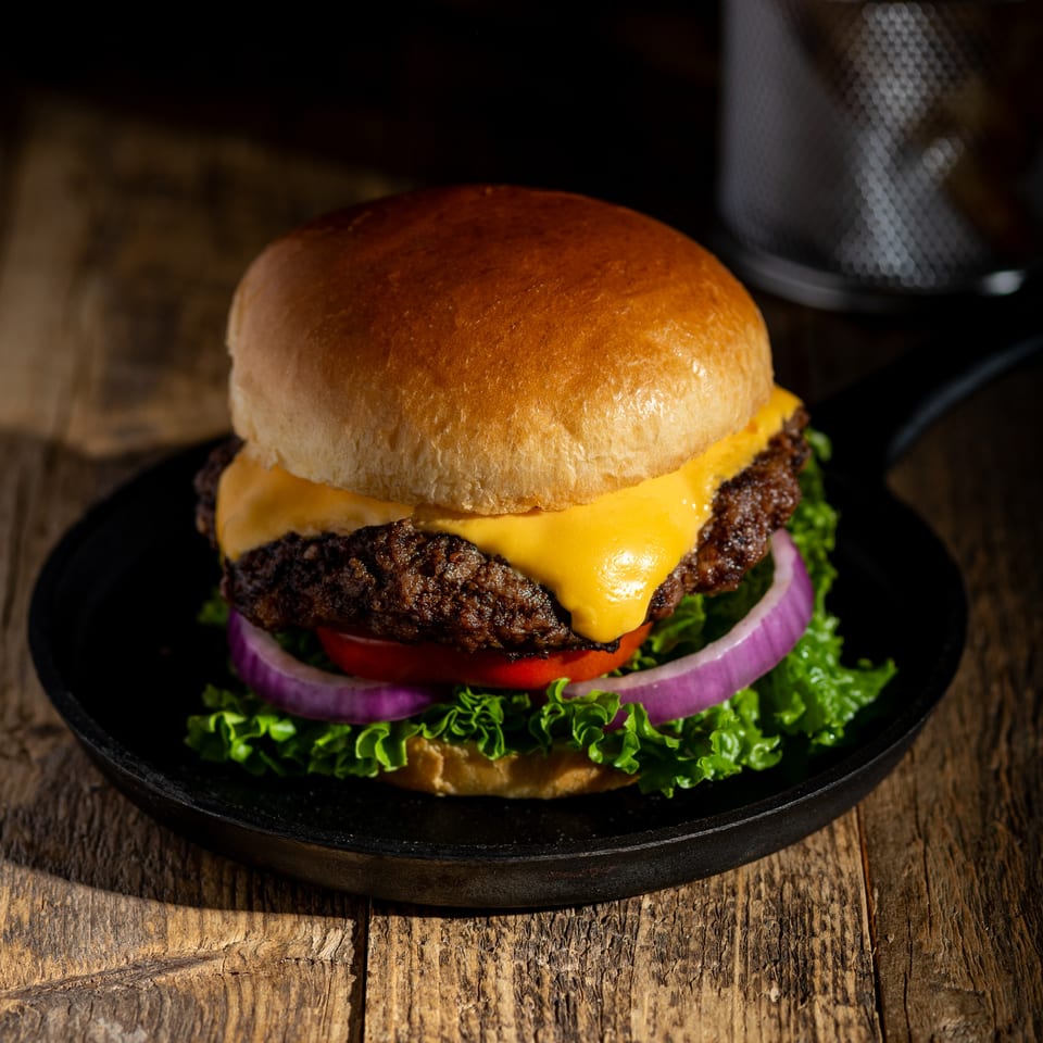 Cheeseburger with lettuce, tomato, and red onion in a cast iron pan on a wooden table.