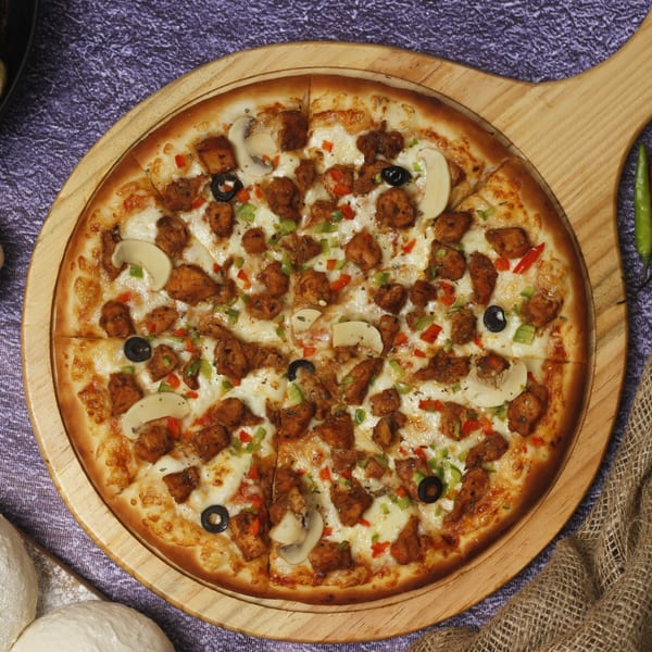 Green Olive Restaurant's Italian pizza, topped with chicken, mushrooms, olives, and bell peppers on a wooden board.