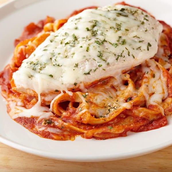 Chicken parmesan with melted mozzarella cheese and parsley on a bed of pasta with red sauce.