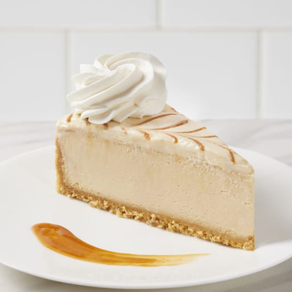A slice of cheesecake with whipped cream and caramel drizzle on a white plate.
