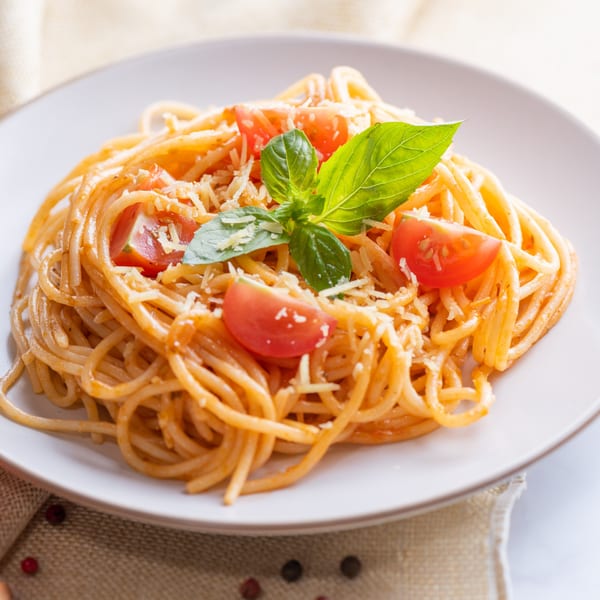 Spaghetti with tomato sauce, grated cheese, cherry tomatoes, and fresh basil on a white plate.