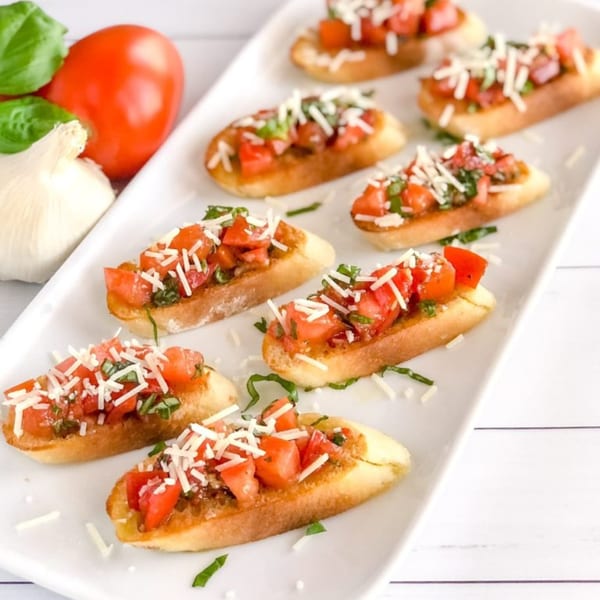 Green Olive Restaurant's bruschetta appetizers with diced tomatoes, basil, and parmesan cheese on a white platter.