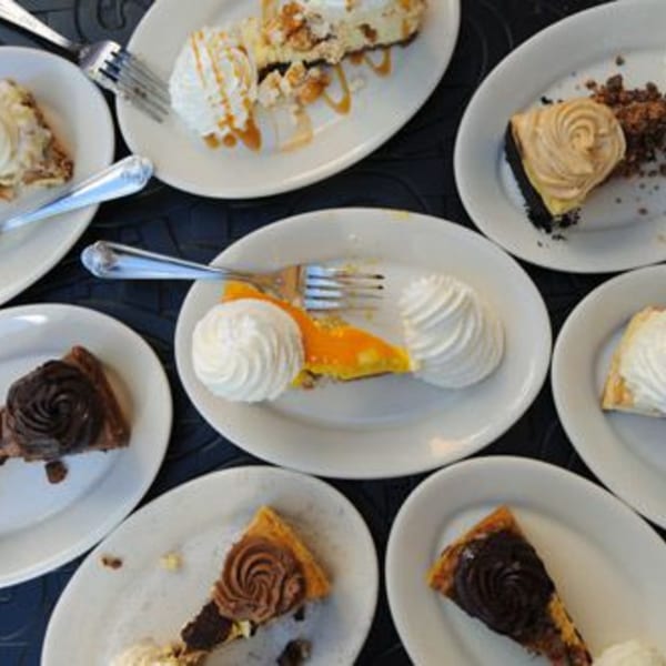 An overhead view of various dessert slices, including cheesecake and chocolate cake, on white plates.